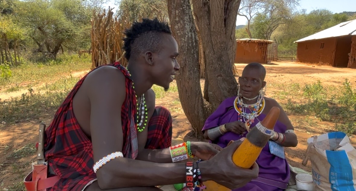 Two Maasai community members talking beneath a tree in the village